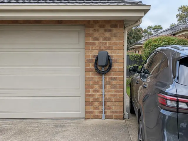 Wall-mounted EV charger on a brick garage wall beside a driveway and car in Rouse Hill