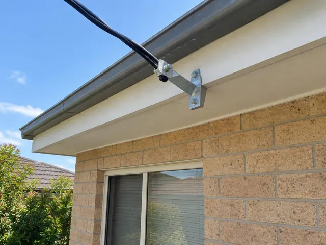 Overhead service cable and point-of-attachment bracket on a brick house eave in Kellyville